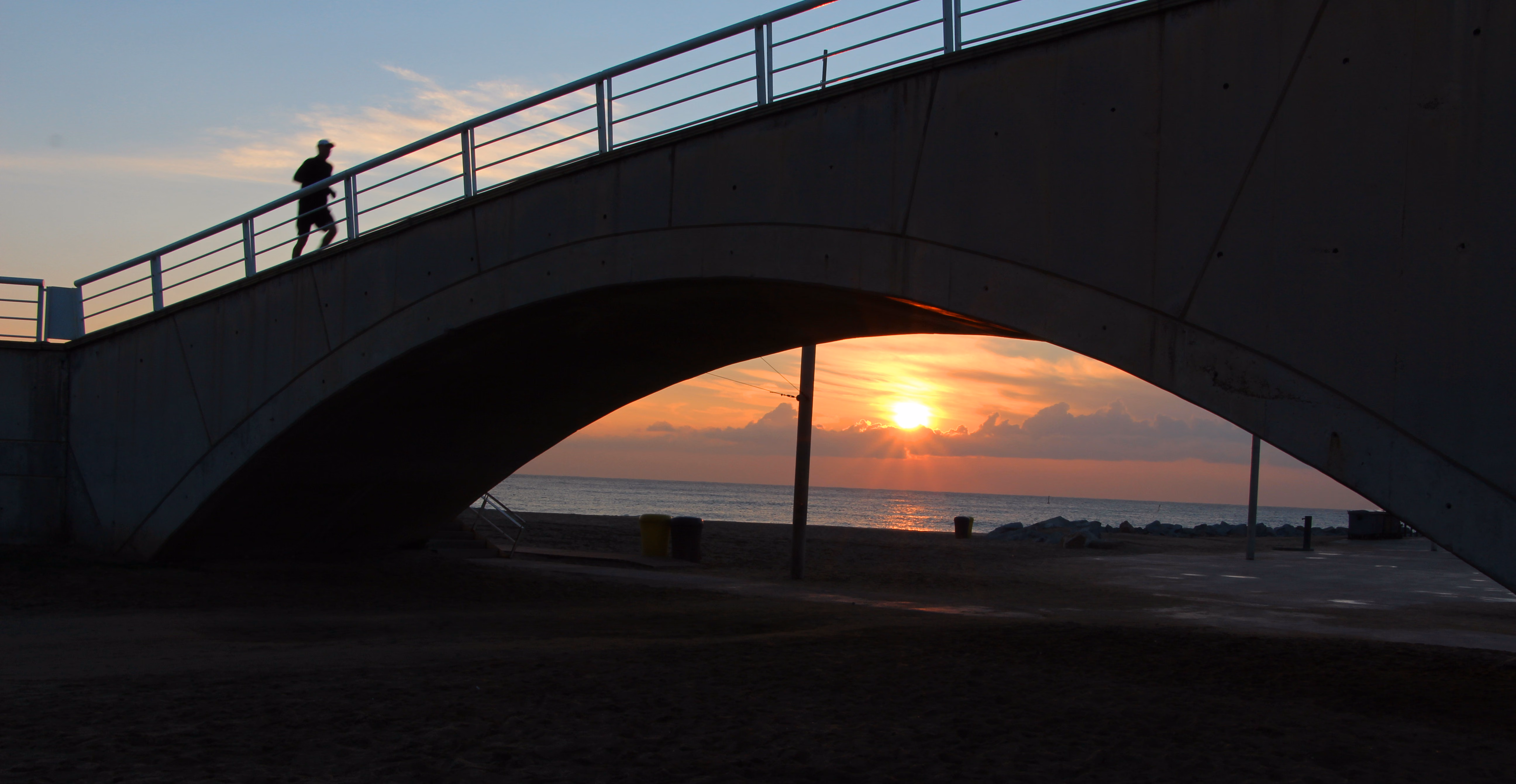 Un corredor cruza un puente peatonal al amanecer, en la playa de Barcelona